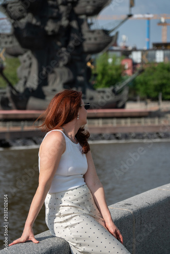 Photography Red-haired woman sits on Muzeon Park embankment near Moscow River with Monument to Peter I blurred behind