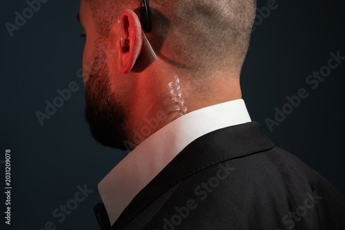 Photos Detailed Close-up Profile View of a Professional Security Agent Wearing a Black Suit, White Collar Shirt, and a Transparent Acoustic Tube Earpiece