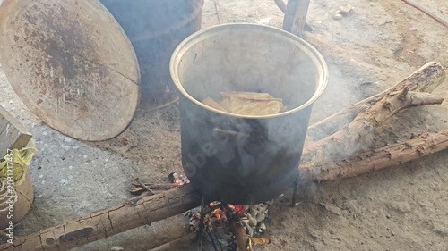Steam and smoke rising from a large metal pot cooking traditional tamales over fire