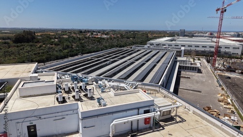Aerial view of a large modern industrial facility with an extensive rooftop solar panel array, boilers, mechanical equipment and a crane

