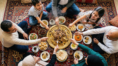 High angle view of a Middle Eastern family gathered around a large platter of traditional Mansaf. Multigenerational Arab family eating together with spoons from a shared dish.
