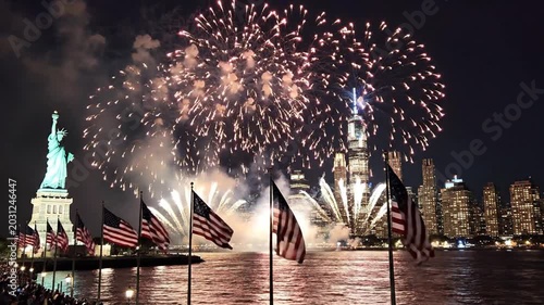 New York harbor at night featuring US flags and white fireworks behind the Statue of Liberty.