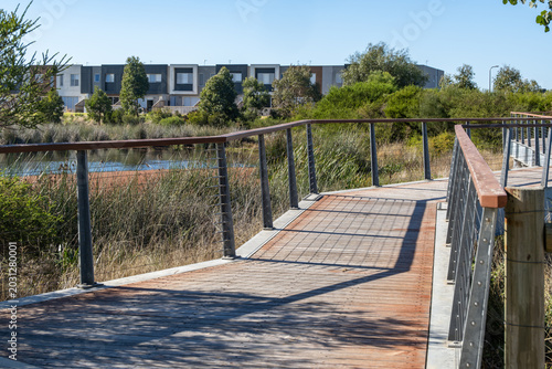 Fotografía A modern timber boardwalk with steel wire handrails snakes over a natural wetlands and reed reserve