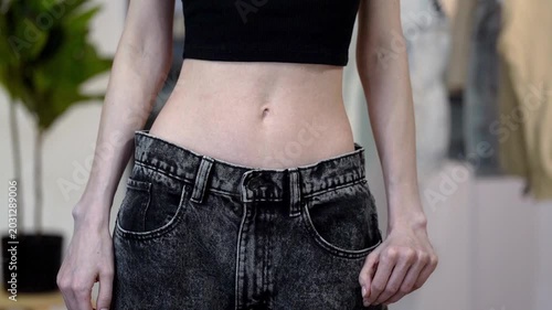 Slim woman releases loose big jeans falling from flat waist after weight loss. Concept of diet success, slimming result, flat tummy stomach, figure change, wellness and clothing size transformation