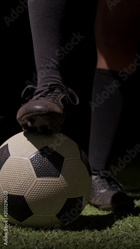 Vertical video: Shifting weight, legs in black socks pressing soccer ball on turf, prepping flick