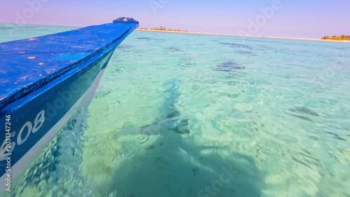Scenic shot of a person relaxing on the bow of a wooden boat cruising through shallow, transparent tropical sea.
