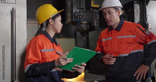 Technicians reviewing machine setup with clipboard in auto parts factory