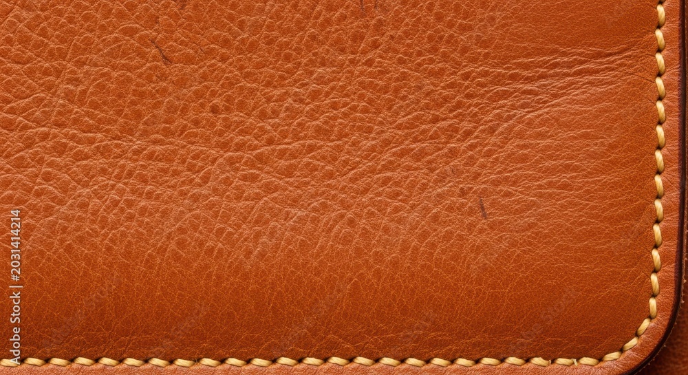 Fototapeta premium Brown pebbled leather texture featuring cream perimeter stitching in a macro sharp focus shot for luxury fashion and upholstery branding