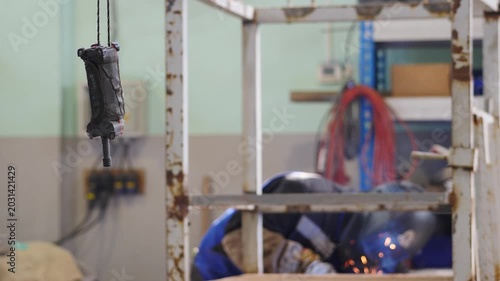 Blurred welder at work shot through crane beam remote control. Industrial settings. factory assembly line with worker in helmet, Metalworking sparks flying, welder working on steel box beam. 4k video