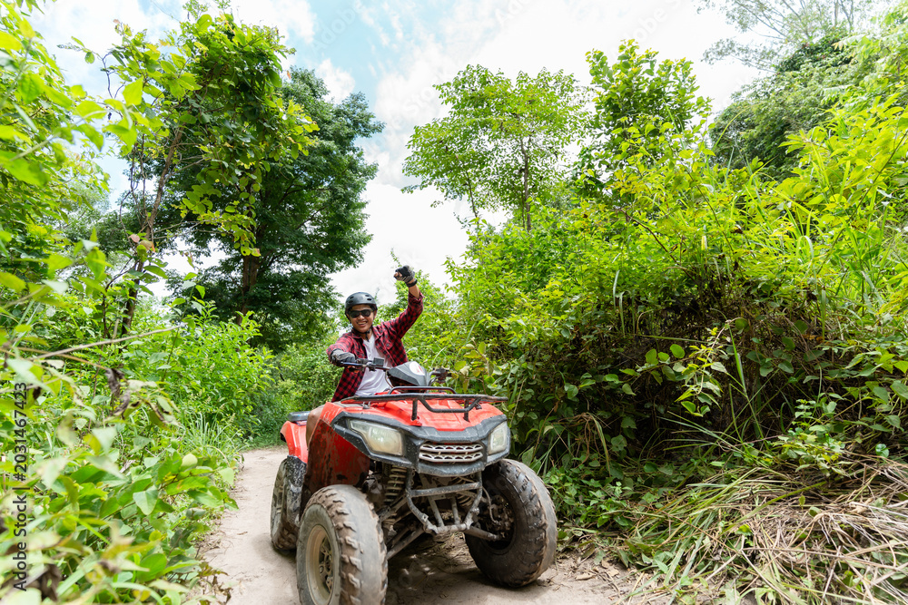 Fototapeta premium Person rides ATV through tropical path in sunny weather with green plants and tall grass around