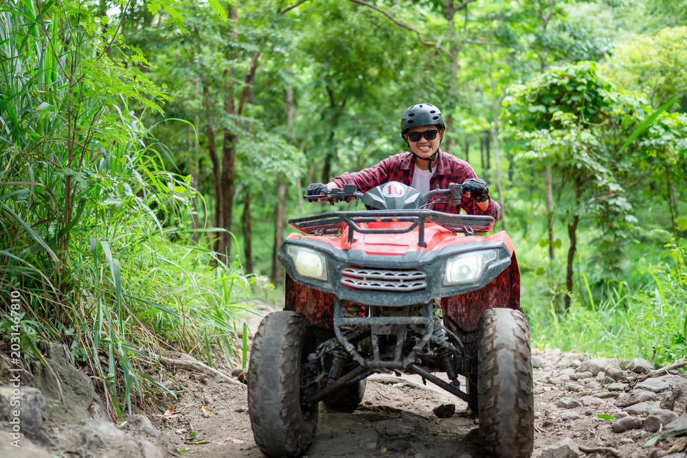 Fototapeta premium Riding an ATV on a dirt trail in the forest with trees and greenery around during the day