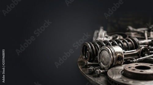Used car engine parts with piston, coil springs, brake disc, and metallic bolts on a table against a dark background, closeup side view copy space.