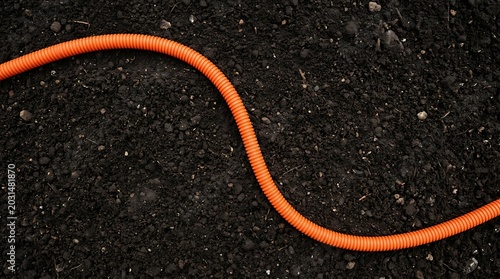 Winding orange electrical cable or hose lying on a dark rough textured surface with electrical, textured