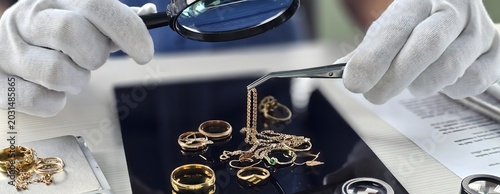 Expert evaluates various gold jewelry pieces with magnifying glass and tweezers