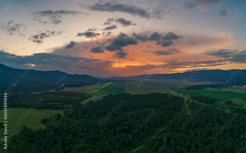 Fototapeta premium Sunset over a winding road through evergreen forests and green fields in the Altai Mountains