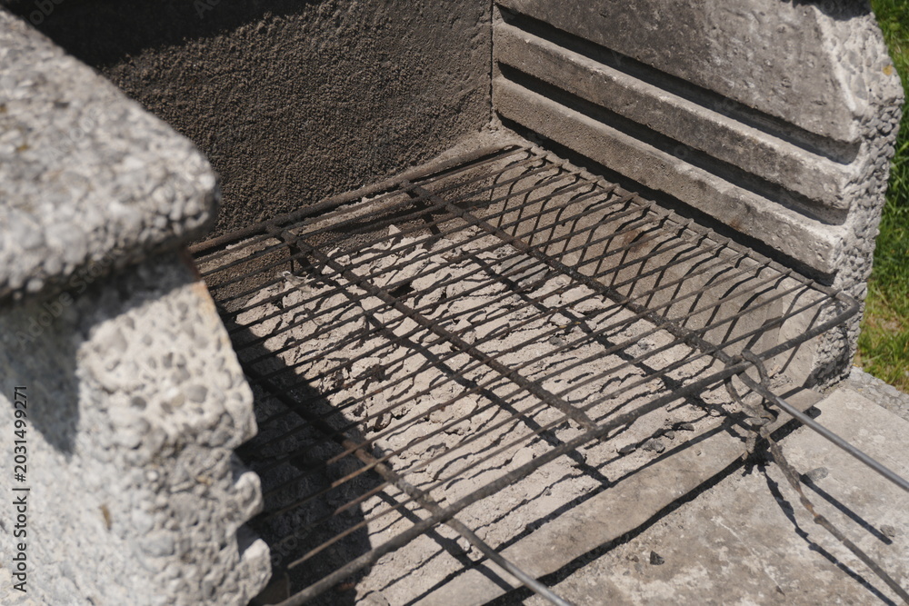 Fototapeta premium Empty Weathered Metal Grill Grate in Rustic Outdoor Concrete Barbecue Pit for Summer Cooking Preparation and Backyard Gatherings