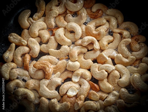 Roasting Cashew Nuts in a Black Pan Close-Up – Slow Motion Style Food Background with Dramatic Lighting, Crunchy Golden Cashews, Dark Moody Kitchen Scene Shot Through a Narrow Opening