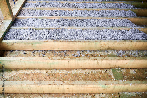 Cellulose paper insulation partially fills floor cavities of timber frame house during installation. Unfinished home construction detail, eco thermal material and energy efficiency concept