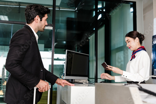 An airline agent scans a traveler's passport at a modern airport check-in counter with a computer on the desk