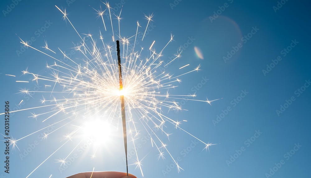 Obraz premium Sparkler, glowing sparks flying, clear blue sky background, symbolizing celebration, joy, and festive spirit