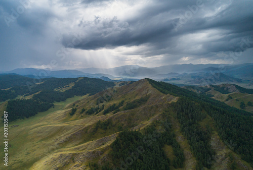 Altai Mountains landscape view with dark storm clouds and sun rays breaking through, illuminating green forest and valleys