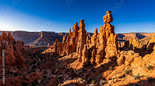 Majestic red sandstone hoodoos stand tall under a bright blue sky in a sunlit desert canyon.
