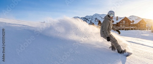 Snowboarder in gray gear speeds down snowy slope with mountain lodge in background at sunset