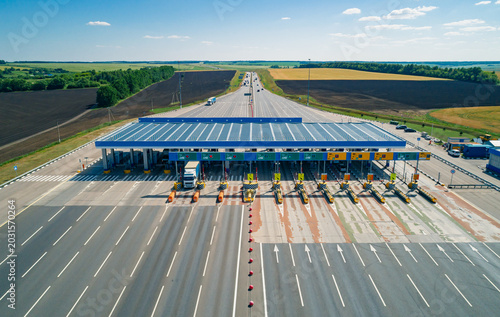 Aerial view of a multi-lane toll station on a wide highway with various vehicles during a sunny day