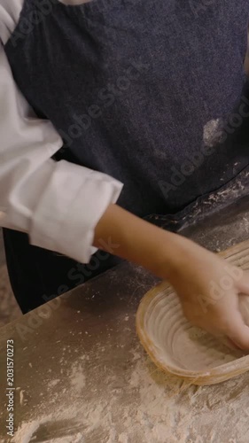 Vertical video: Dusting bench baker forming dough for proof in bakery with bannetons in blue apron