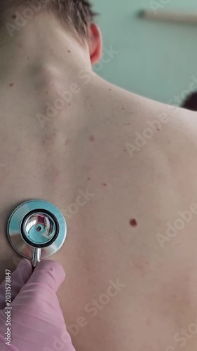 Doctor checks patient back with stethoscope in clinic setting during daytime