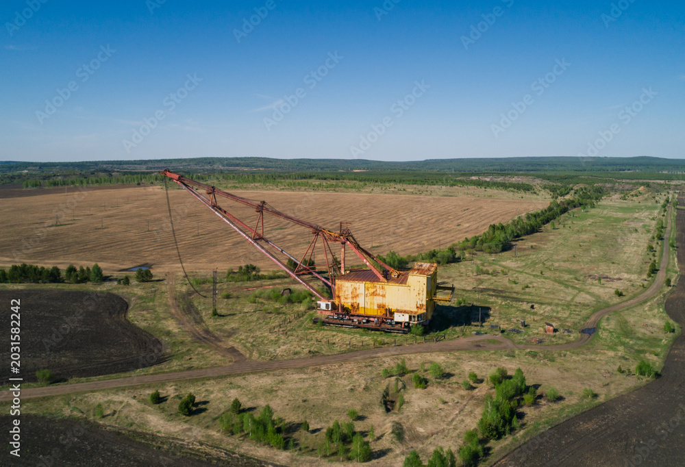 Fototapeta premium Massive industrial dragline excavator rests in an open field, surrounded by sparse vegetation and dirt roads