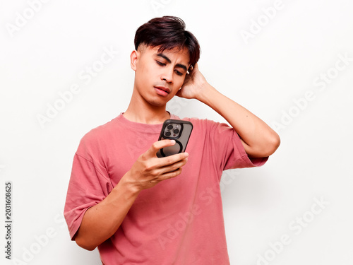Confused young Asian man looking at smartphone screen while scratching his head with doubtful expression isolated on white background