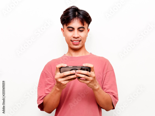 Happy young Asian man holding smartphone horizontally and looking at screen with smile, enjoying mobile game or watching streaming video content on isolated white background.