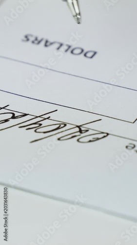 Close-up of hand signing US paper check with pen. Vertical composition capturing financial transaction, payment process and professional banking documentation detail.