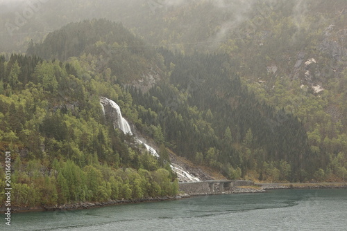 Furebergsfossen Waterfall.  A view of Furebergsfossen a glacier fed waterfall.  The waterfall flows under the road and directly into the Maurangerfjord, an arm of the Hardangerfjord in Norway.