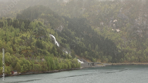 Furebergsfossen Waterfall.  A view of Furebergsfossen a glacier fed waterfall.  The waterfall flows under the road and directly into the Maurangerfjord, an arm of the Hardangerfjord in Norway.
