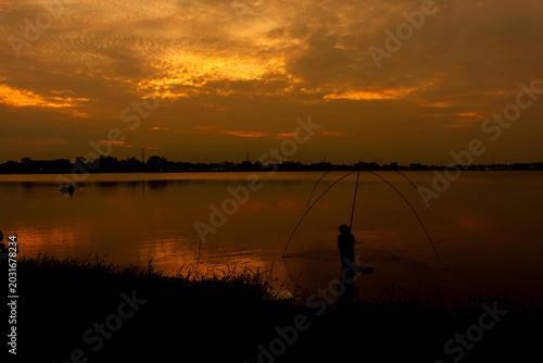 Silhouette of a traditional fisherman with a dip net in a lake at sunset.