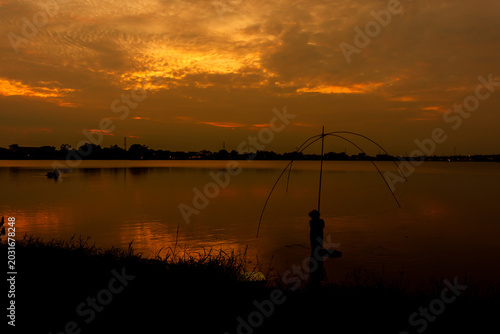 Silhouette of a traditional fisherman with a dip net in a lake at sunset.