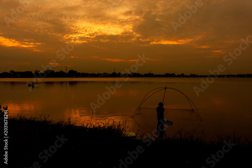 Silhouette of a traditional fisherman with a dip net in a lake at sunset.