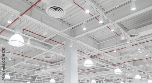 Industrial building ceiling with exposed pipes, ventilation, and modern lighting fixtures showcasing internal infrastructure.