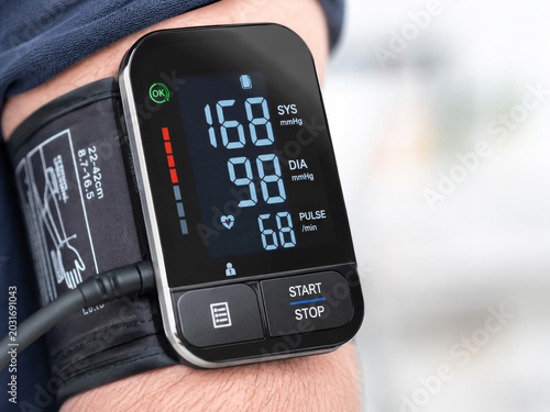 Close-up of a modern digital blood pressure monitor on a person's arm, displaying concerningly high systolic and diastolic readings (168/98 mmHg) and pulse rate, indicating potential hypertension or h