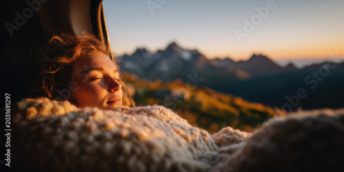 Woman resting on cozy blanket as sun sets over the mountains