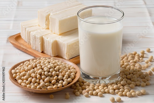 Tofu blocks soy milk in glass and soybeans on white wooden table