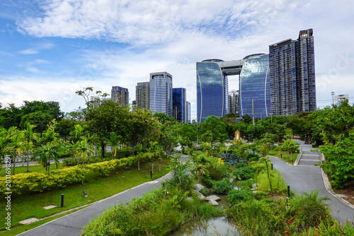 Quadro su tela This green urban park in Bangkok, Thailand, surrounded by skyscraper views and a clear blue sky on a sunny day, reflects the sustainable coexistence of the capital city and nature