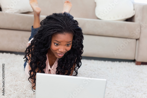 Fotografie African American woman lying on shag rug using silver laptop, wearing sleeveless