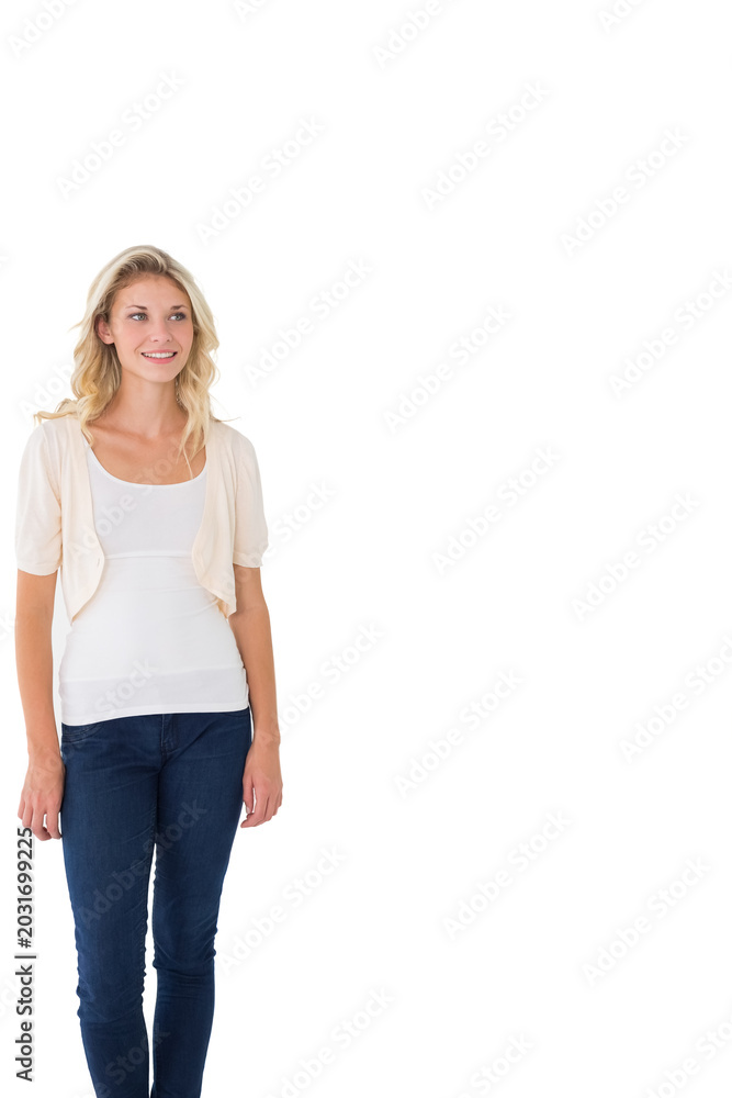 Fototapeta premium Woman in 20s standing left studio in white tank cream cardigan jeans gazing upper-right, copy space