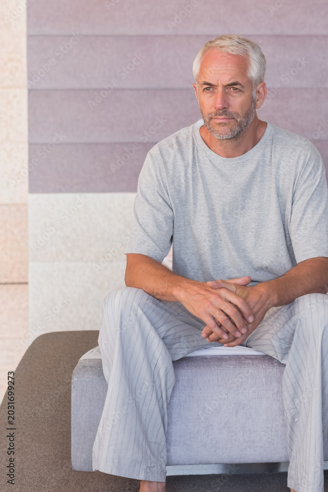 Fototapeta premium Man sitting on low ottoman wearing gray tee and striped pants inside lobby with tiled wall