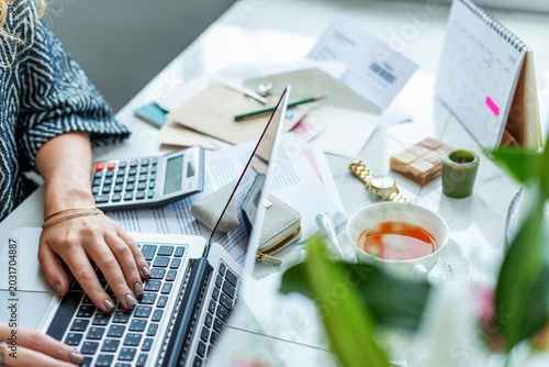 Foto Person typing on a laptop at a cluttered desk with tea and papers