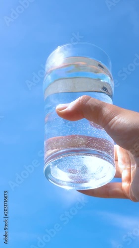 transparent glass glass of water with pure mineral water in hand against the sky with bright glare of the sun