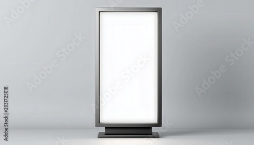A modern, vertical digital advertising display with a blank white screen stands against a plain gray wall and floor.
